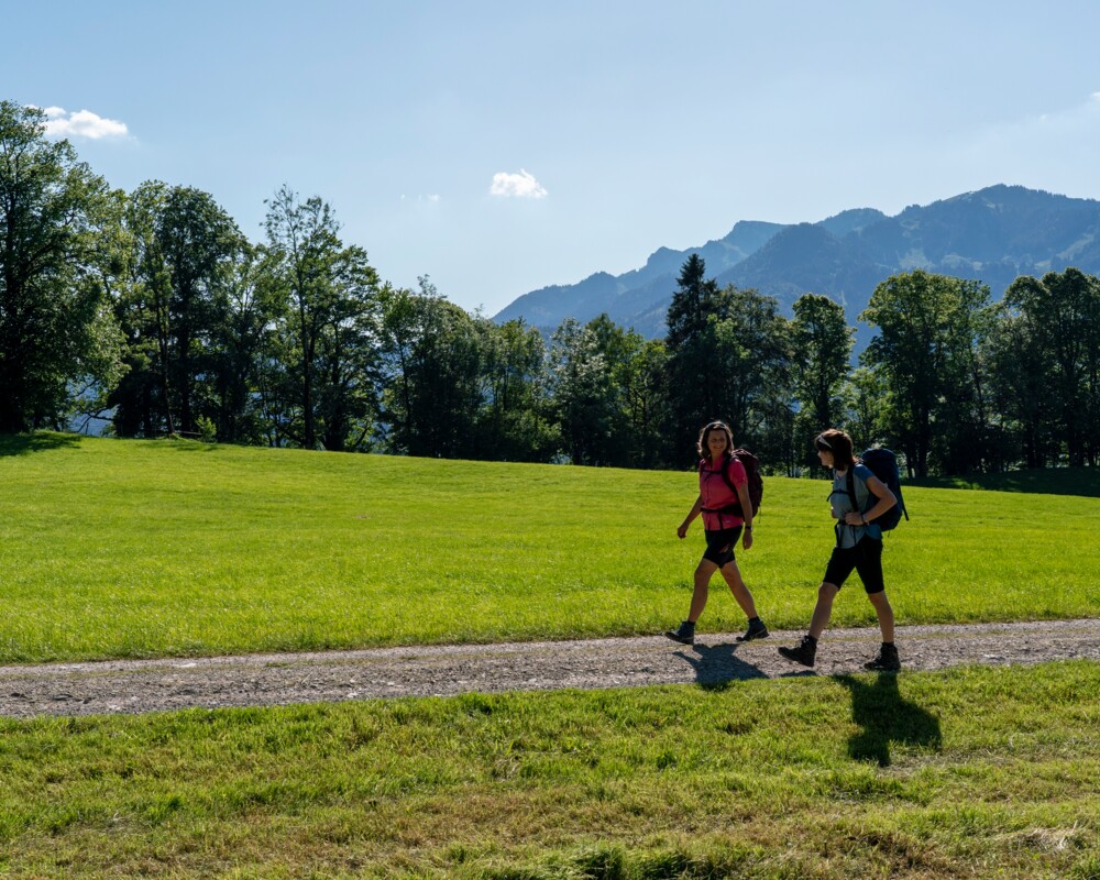 Zwei Frauen beim Wandern unterwegs von Mühlbach nach Lasseln mit Brauneck im Hintergrund