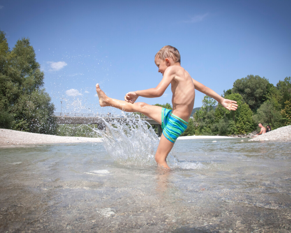 Ein Junge spritzt Wasser in der Isar