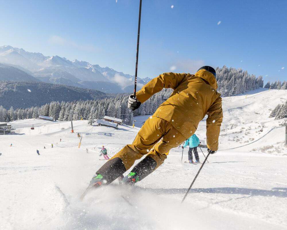 Skifahrer auf der Piste und hinter Ihm wirbelt Schnee auf