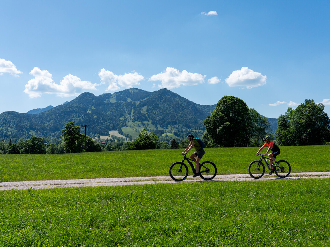 Zwei Radfahrer mit Brauneck im Hintergrund