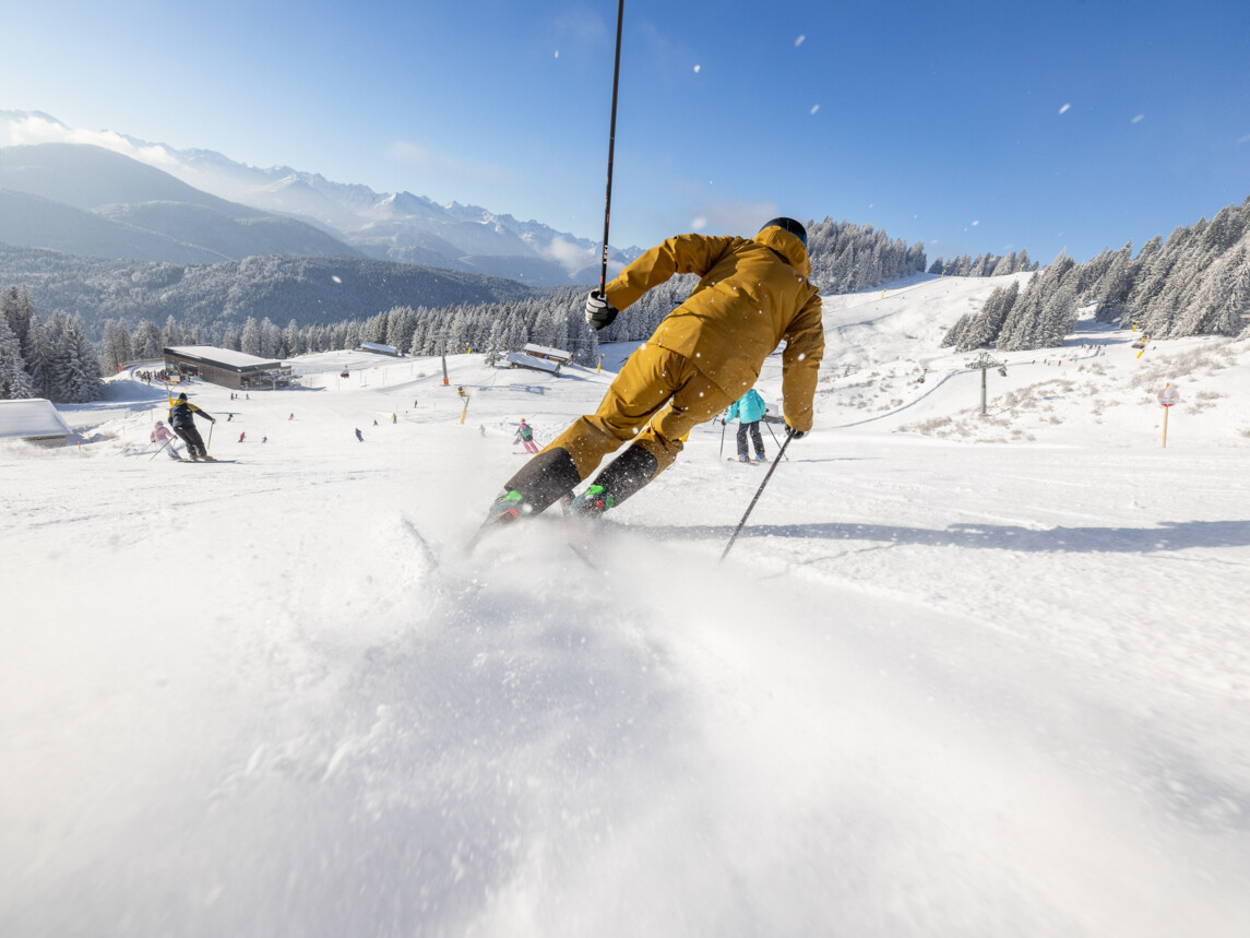 Skifahrer auf der Piste und hinter Ihm wirbelt Schnee auf