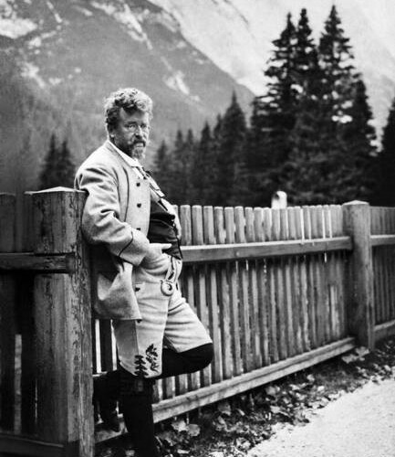 ein Schwarz-weiß Foto mit einem Mann in Tracht der an einem Zaun sich anlehnt