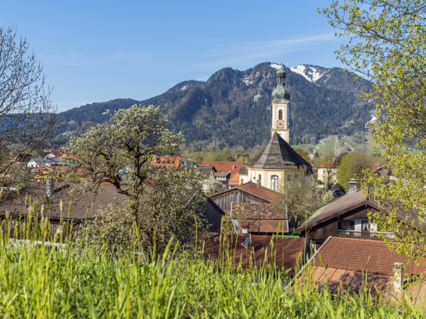 Ortsansicht mit Kirche und Brauneck im Hintergrund im Sommer