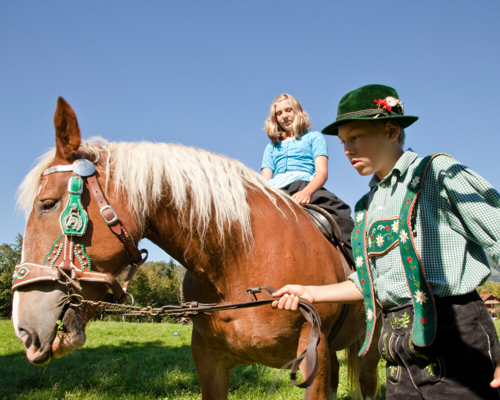 Ein Junge in Tracht führt ein Pferd mit reitendem Mädchen