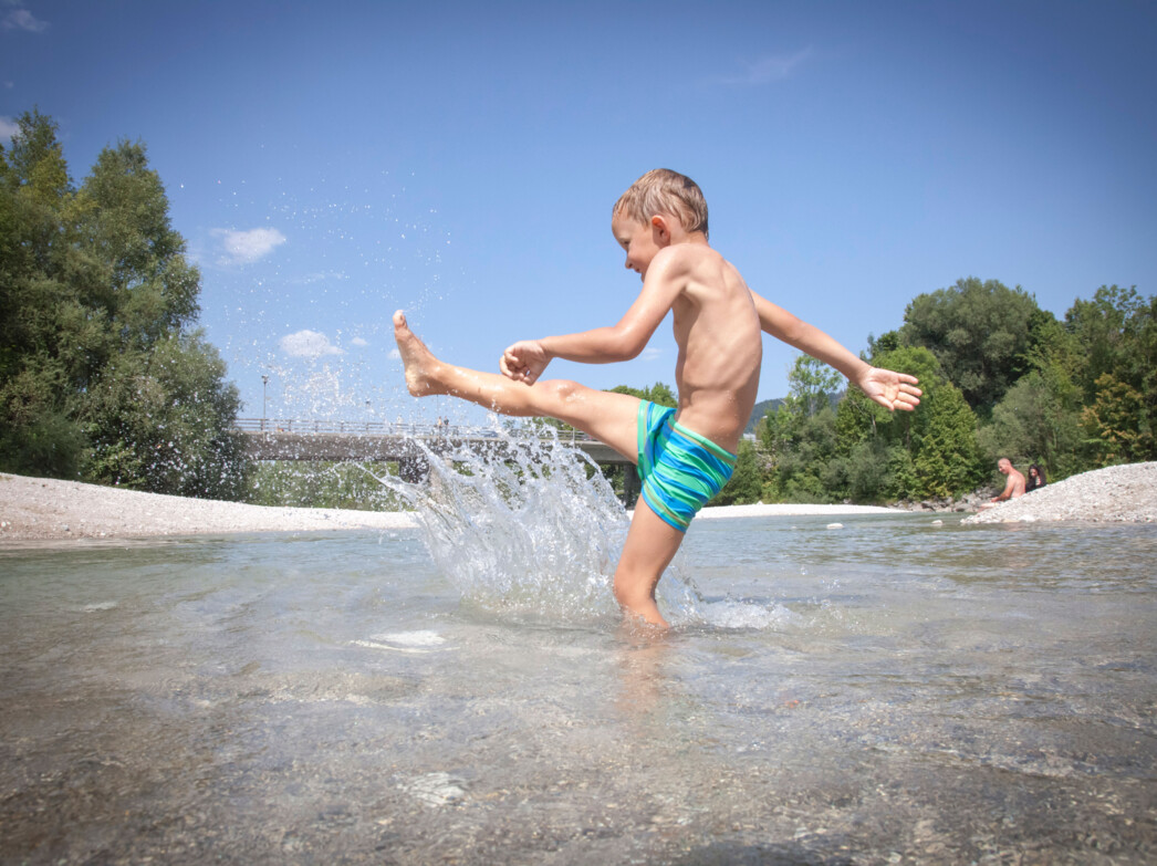 Ein Junge spritzt Wasser in der Isar