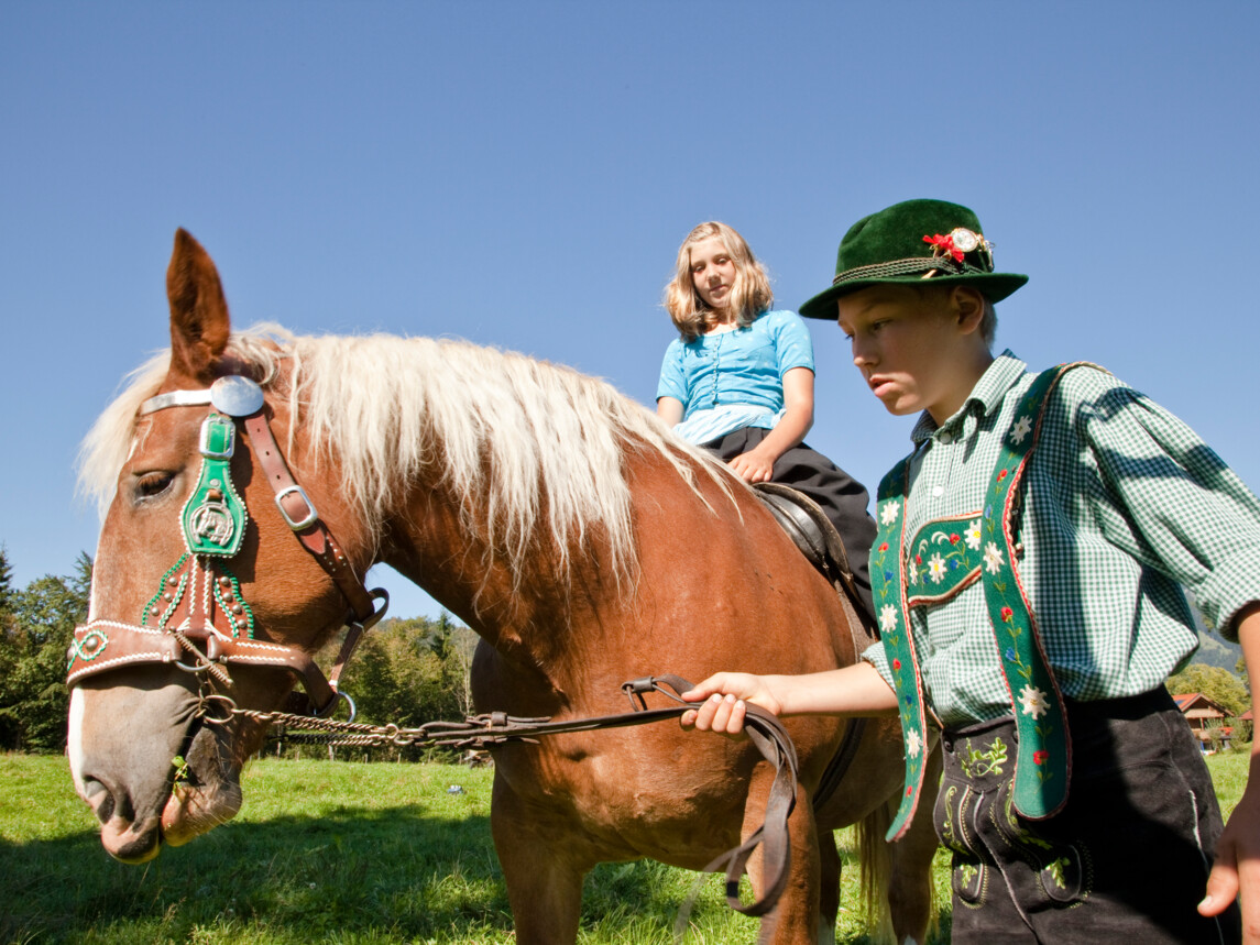 Ein Junge in Tracht führt ein Pferd mit reitendem Mädchen