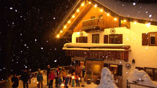 unbekannt, Laternenwanderung die Reiseralm ist beleuchtet, davor viele Menschen mit Laternen und Schneesachen an, denn es schneit dicke Flocken