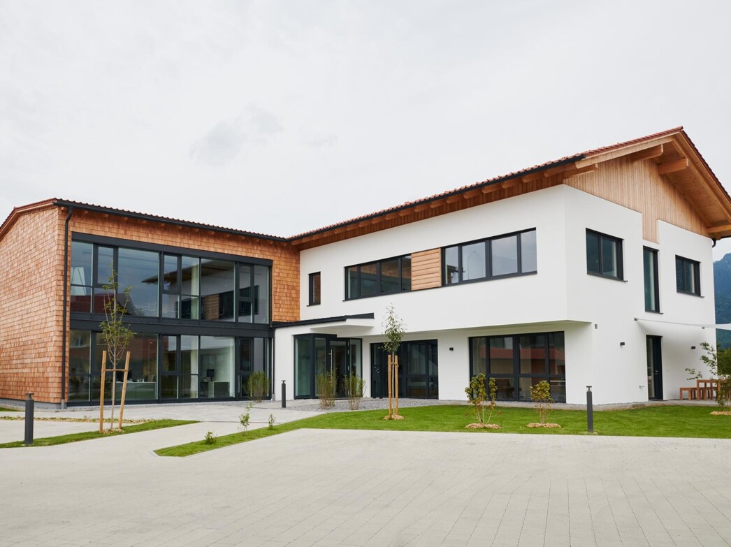 eine Tasse mit Kaffe ist im Vordergrund und daneben ein Stück Kuchen auf einem Teller. Nebenan ist ein Glas Wein und weitere Tassen auf einem Tisch mit einer roten Tischdecke