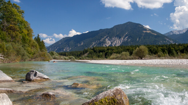 Die Isar bei strahlendem Sonnenschein und türkis - blauen Wasser und eine Aussicht auf die Berge