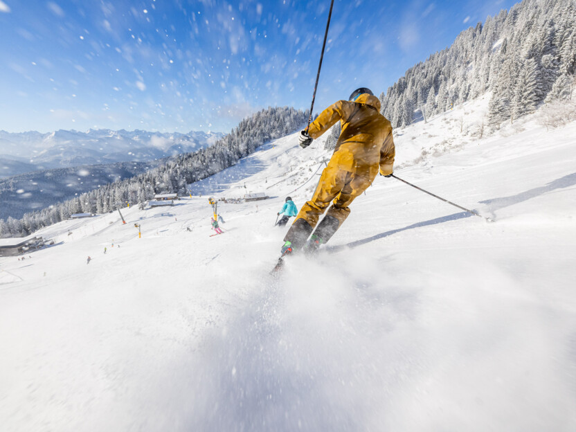 Skifahrer bei perfekten Bedingungen – im Vordergrund wirbelt eine Schneewolke auf.